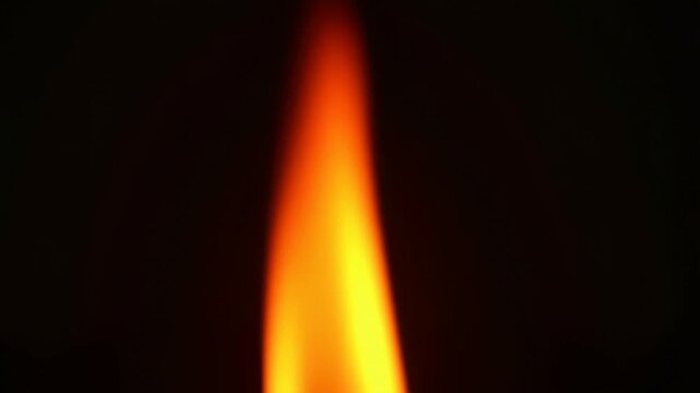 Glowing candle flame in darkness: flickering light and warmth in a dark setting