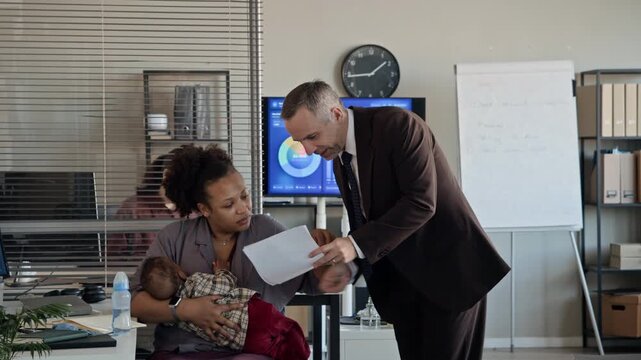 African American woman holding baby while discussing documents with Caucasian middle aged male colleague in office. Video perfect for corporate diversity and working mother campaigns