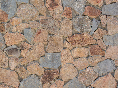 a decorative retaining wall built from natural split stones of different sizes with brown, orange and gray inclusions, tightly bonded together with durable gray concrete mortar joints