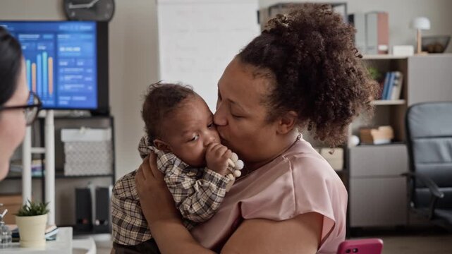 Middle aged Caucasian businessman and African American mother holding baby talking with colleague in office. Video ideal for family friendly workplace policies and diversity in corporate culture