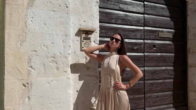 Glamorous Woman Posing Next to Ancient Carved Doorbell on White Stone Wall Matera Italy