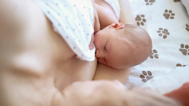 Newborn baby latches onto the mother's breast, feeding from her loving arms while lying in bed, illustrating a tender moment of bonding, nourishment, and essential infant care