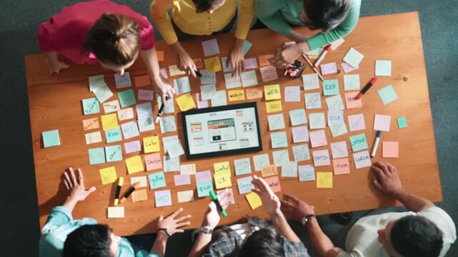 Top view of smart developer working on tablet display website wireframe prototype for mobile phone while putting hands together to celebrate successful project. Team making stack of hand. Symposium.