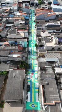 Imagem a&eacute;rea mostra rua ornamentada com pinturas inspiradas na Sele&ccedil;&atilde;o Brasileira para a Copa, refletindo uni&atilde;o comunit&aacute;ria e valoriza&ccedil;&atilde;o da cultura esportiva.