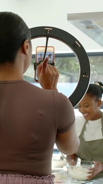 Vertical video: Tapping operator adjusting ring and filming baker in apron stirring bowl in kitchen