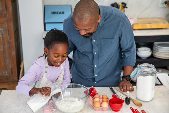 African American father and daughter pouring milk into large glass bowl at home kitchen counter
