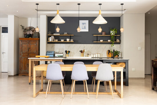 Wooden dining table, four gray chairs occupying center in open kitchen showing pendant lights