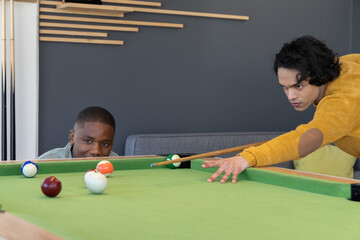 Obraz premium Diverse male friends playing pool at recreation lounge on green felt table with cue stick