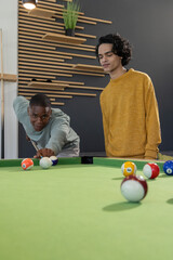 Obraz premium Diverse male friends leaning, taking shot on green pool table in modern lounge with cue