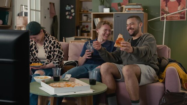 Diverse young adults sitting on sofa, eating pizza, drinking soda, and laughing while watching standup or comedy on television. Fast food delivery campaign, student lifestyle or entertainment promo
