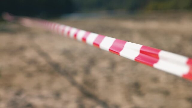 Closeup view of red white striped barrier tape marking restricted area at construction site. Safety warning tape blocks access to dangerous zone