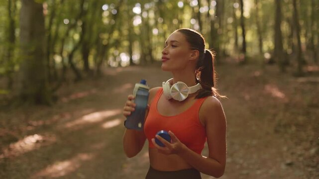 Woman drinking water after jogging in forest, staying hydrated and recovering from her workout while enjoying fresh air and nature, 4K