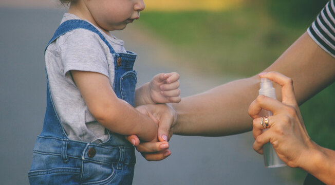 Mother spraying mosquito repellent on her toddler's skin outdoors