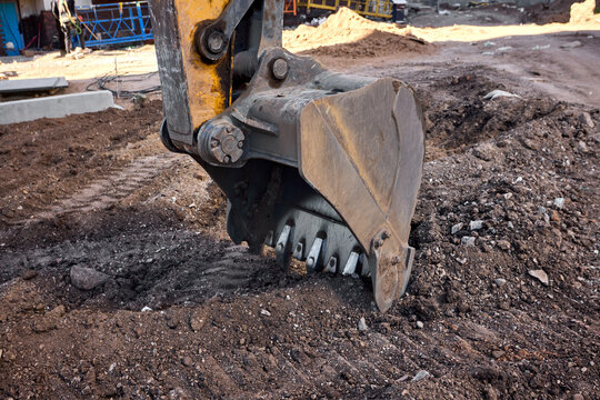 Excavator bucket digging into urban construction site soil
