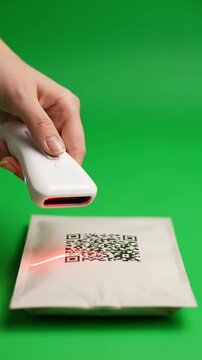 Hand scanning QR code on package with laser scanner on green background.