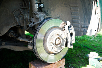 Fototapeta premium Close up of a car wheel assembly with exposed brake disc, caliper, suspension parts and tire on a jack stand outdoors in daylight, showing vehicle maintenance