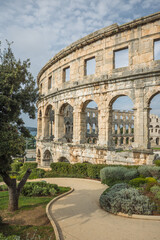 Naklejka premium The Pula Arena, a Roman amphitheatre. The historic stone arches and walls show the grandeur of ancient architecture. A winding path lead towards the colossal structure. Pula, Croatia.