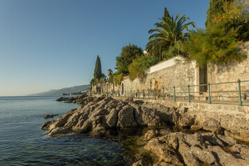 A scenic view of the coastal Lungomare promenade with a stone wall and green railing next to the rocky Adriatic Sea shore. Opatia, Croatia. © petrsvoboda91