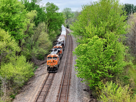 Savanna, Illinois - USA - April 24, 2026; Aerial view of a BNSF  railroad locomotive pulling a freight train of cars along the forested bluffs of the  Mississippi river