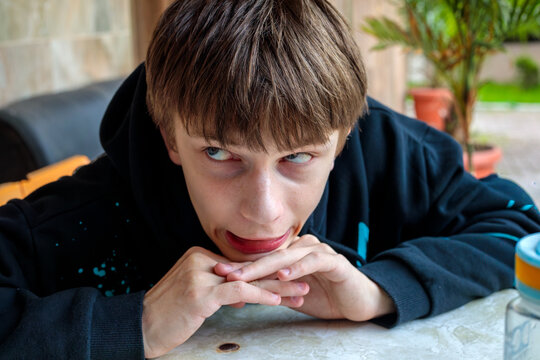 Teenage boy in black hoodie staring intensely at camera with suspicious narrowed eyes and slight smirk, moody candid teen portrait outdoors