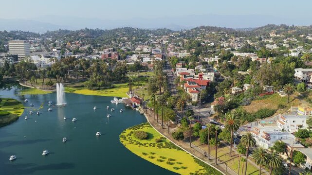 Scenic aerial of Echo Park Lake in Los Angeles revealing swan boats, large fountain, surrounding neighborhood with lush greenery, hills, urban landscape