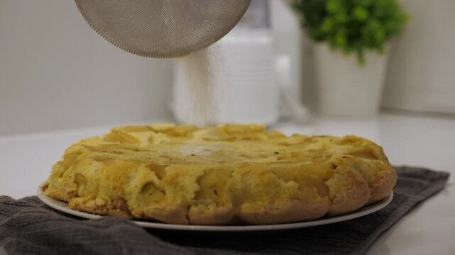 Cooking charlotte. Sprinkling powdered sugar on the pie. Freshly baked pie, finishing touch before serving. Closeup
