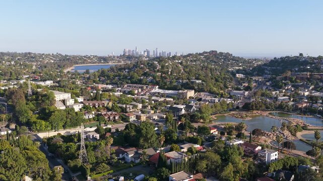 Rowena Reservoir in Silver Lake neighborhood, distant Downtown Los Angeles skyline, on a clear sunny day with residential suburban houses and trees