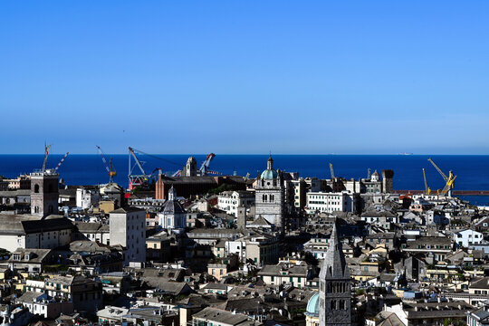 aerial view of Central Genoa port area. rooftops and stucco facades. heavy duty harbor cranes in a distance. church towers and dome. deep blue sea at the horizon. travel and tourism concept.