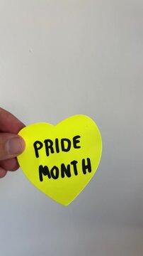 Hand holding heart shaped pride month note on white background