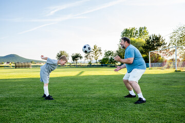 Obraz premium Father teaching son football skills during training on sports field.