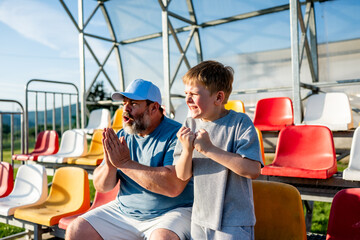 Father and son cheering for football team during match at stadium.