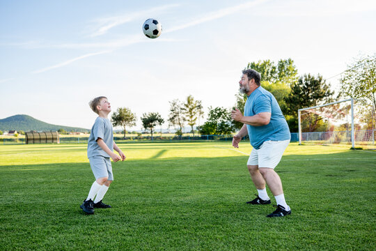 Father teaching son football skills during training on sports field.