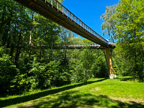 germany, impressive wooden bridge architecture rising through forest canopy beneath brilliant blue sky in public park