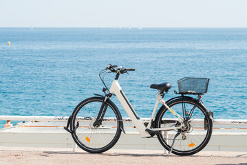 Fototapeta premium Modern electric bicycle parked on a sunny seaside promenade, overlooking the deep blue sea during a summer vacation.