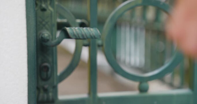 Man Opening and Closing Ornate Green Metal Garden Gate