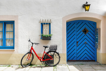 Fototapeta premium Red bicycle against the facade of a building with blue wooden door and windows in Fussen, Bavaria, Germany