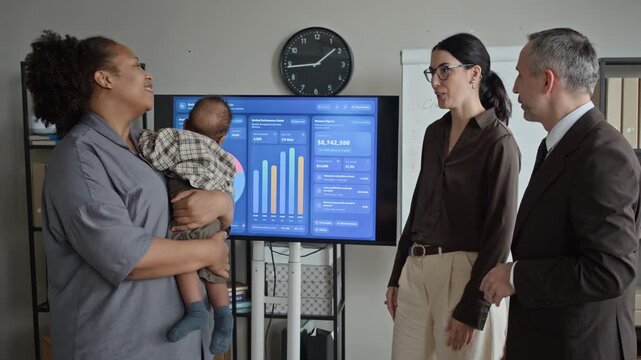 African American woman holding baby infant, walking to office desk and writing in notebook. Clip suitable for promoting work-life balance and family-friendly corporate policies