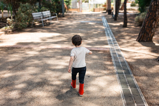 Young boy exploring park in red boots