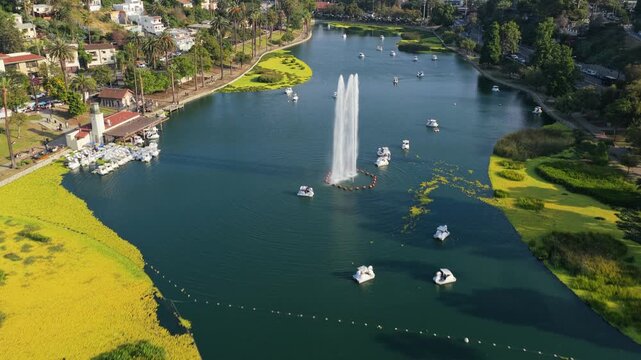 Scenic flight above Echo Park Lake featuring paddle boats, central fountain, iconic downtown Los Angeles skyline revealing famous skyscrapers during daytime