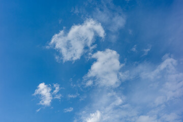 Fototapeta premium Clouds float in a clear blue sky during the day with sunlight shining from above in an outdoor scene