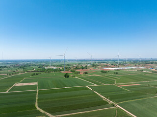 Naklejka premium Wind turbines standing in green agricultural fields under a clear blue sky
