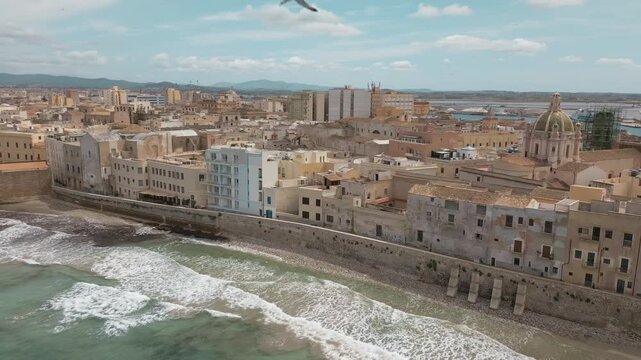 Trapani, Sicily Aerial Panoramic Panning Overview of City and its Sea Wall, Church and Harbor with Seagulls flying overhead on warm sunny day in 4k