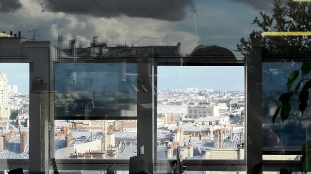 Espace de bureau moderne avec vue panoramique sur les toits de Paris &agrave; travers une baie vitr&eacute;e