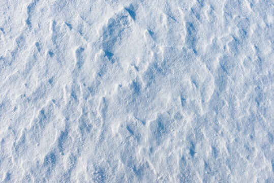 High angle view of textured snow surface with wind patterns and blue shadows. Winter snow texture background banner representing frosty weather, cold climate and clear space.