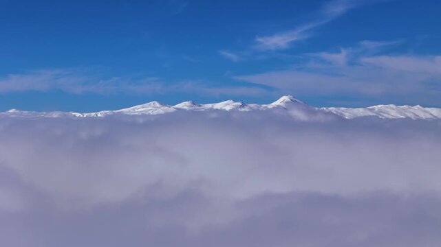 Cinematic drone reveal shot of a majestic snowy mountain peak emerging through thick clouds and mist in winter. t&uuml;rk&ccedil;rsi nedir