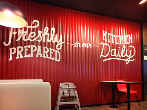 The interior of a KFC fast-food restaurant. The walls are covered with red metal panels featuring white lettering: Abakan, Russia - June 10, 2026