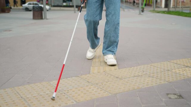 Visually impaired man walking with a cane on tactile paving