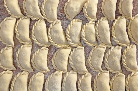 Freshly made vareniki dumplings prepared for cooking on wooden board, top view
