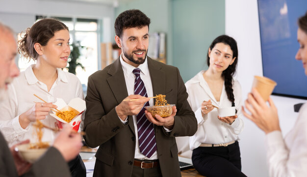 Group of friendly young office workers different ages standing and eating fast food at bright modern office canteen