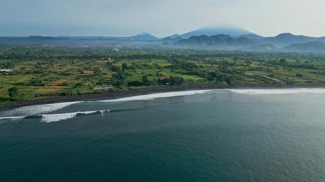 Wide aerial bay panorama with calm surf, green hinterland and distant volcanic silhouettes sweeping drone footage for tourism campaigns, coastal conservation visuals and serene,Bali island,Indonesia
